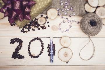 2018 inscription of coffee beans, shiny purple christmas decorations, a skein of threads on a light wooden background, top view