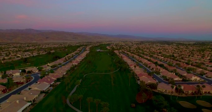 Tracking aerial shot descending over a suburb an golf course at dusk
