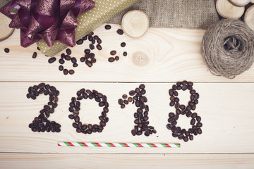 2018 inscription of coffee beans, a gift box, wooden slices, a christmas straw and a skein of threads on a light wooden background, top view