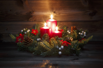 Third Advent - Decorated Advent wreath with three red burning candles on a wooden background with festive atmosphere