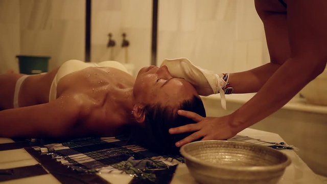 masseur is cleaning face skin with kese bath mitt of client woman, is lying on a table in a hammam
