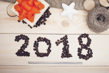 2018 coffe beans inscription, a toy star, a gift box with an orange bow, light wooden background