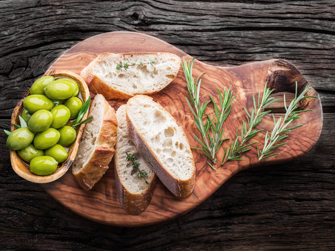 Slices of ciabatta with olives and spices on the serving wooden tray.