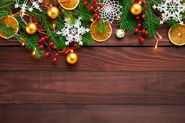 Christmas background decoration with lights, snowflakes, gold balls and fir tree flat lay on dark wooden texture. Top view with blank space.