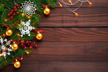 Christmas background decoration with lights, snowflakes, gold balls and fir tree flat lay on dark wooden texture. Top view with blank space.