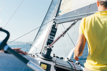 Professional sailor or yachtsowner controls sailboat with mainsail and spinnaker up, by observing...