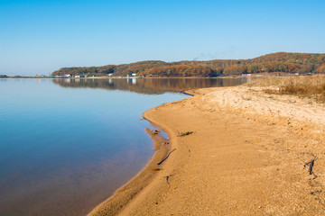Sandy shore near smooth lake surface.