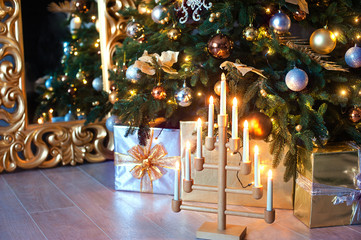 beautiful Christmas interior. A Christmas tree with gold ornaments, boxes with gifts, and a candelabrum with burning candles.