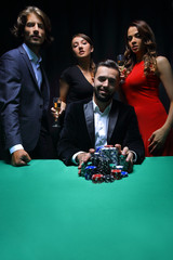 People standing at the table, looking, while a person is betting