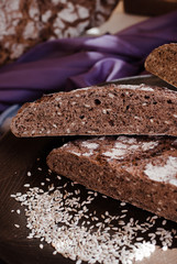Cut loaf of dark farmhouse rye bread with sun flower seeds, flaxseed and floured crust on dark wooden background and sunflower seeds