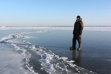 Man in warm clothes walking along the thin ice of a frozen river in the evening, Ob reservoir, Siberia