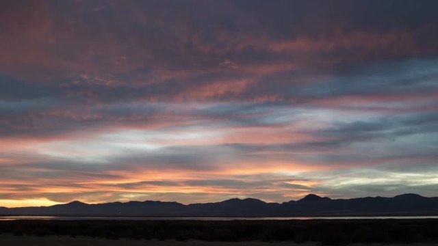 Time lapse viewing wave of color moving through the clouds during vibrant sunset over the open range.