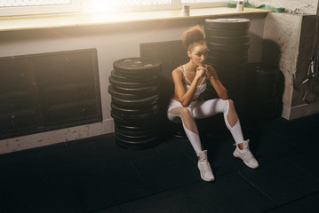 Fit power athletic confident young woman crossfit trainer. The girl sits on the weights plates for the barbells and thinks about the record. Fashion show concept. The ideal sports coach.