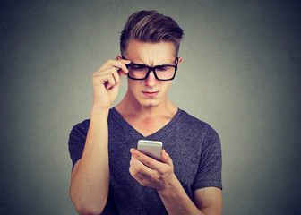Closeup portrait of a man wearing glasses having trouble seeing cell phone has vision problems. Confusing technology