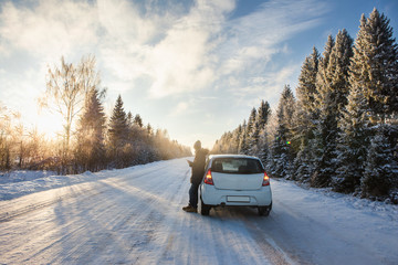 A man with a phone is standing by the car on a winter road