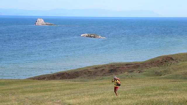 Hiking woman with backpack walking along the road near the blue lake Baikal.