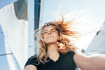 Young beautiful blonde woman makes selfie on sailboat or yacht, wind blows hair