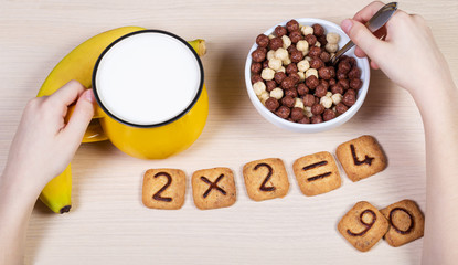 Healthy food for a school children. Milk, banana and funny cookies with numbers. Child has breakfast and does sums using biscuits. Idea of easy arithmetics during eating.