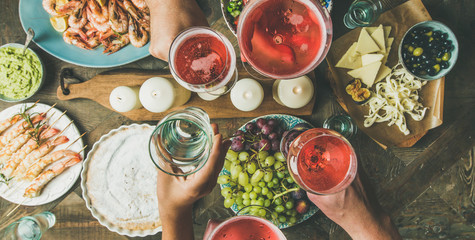 Holiday celebration table setting with food. Flat-lay of friends hands eating and drinking together. Top view of people having party, gathering, celebrating with rose champaign, wide composition
