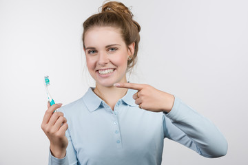 Junge Frau zeigt auf ihre Zahnbürste und lächelt