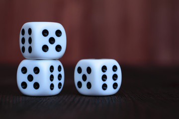 Stack of three white plastic dices on brown wooden board background. Six sides cube with black dots. Numbers 5, 6.