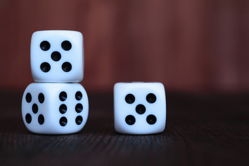 Pile of three white plastic dices on brown wooden board background. Six sides cube with black dots. Numbers 5, 6.