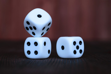 Stack of three white plastic dices on brown wooden board background. Six sides cube with black dots. Numbers 1, 2, 4 and 5.