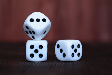 Pile of three white plastic dices on brown wooden board background. Six sides cube with black dots. Numbers 1, 3 and 5.