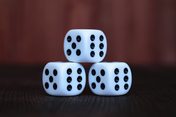 Pyramid of three white plastic dices on brown wooden board background. Six sides cube with black dots. Numbers 5 and 6.