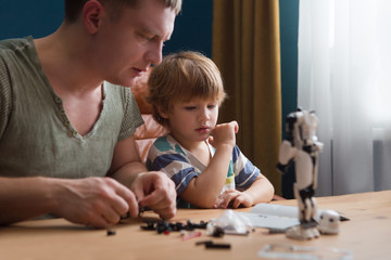 Fototapeta premium Family and childhood concept. Father and his little son play together plastic blocks and makes robot. 