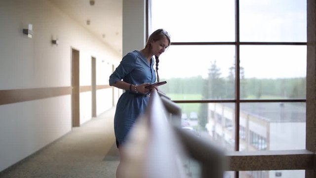 The young woman in the hallway of hotel, waved hand, greets her friends who are on the lower floor.