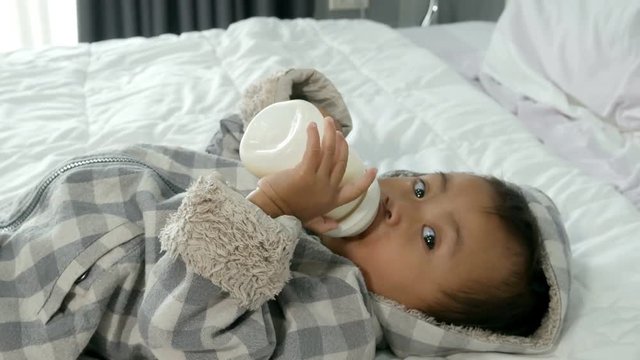 4k of Cute baby drinking milk a bottle in white bed