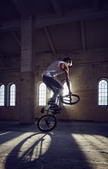 BMX stunt and jump riding in a hall with sunlight.