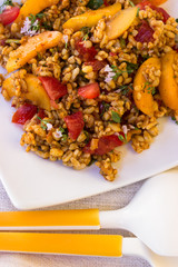 Bulgursalat mit Pfirsich und Tomaten auf einem weißen Teller mit Salat-Besteck