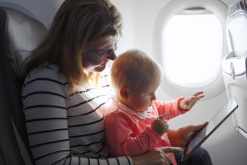Fototapeta premium Mom and child playing tablet while flying on plane
