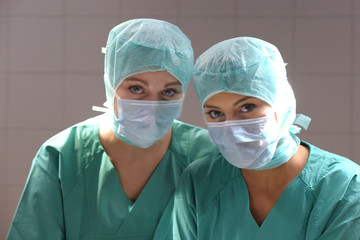 Two young women pose in a low lit operation theater.  Fully dressed as theater nurses with face...