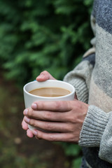 Hands holding a cup of warm coffee in a forest