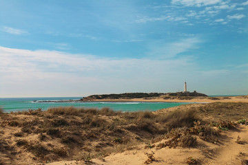 Fototapeta na wymiar Panoramic view of the beach of Los Canos de Meca, with the Cape of Trafalgar in the background, and the lighthouse of Trafalgar, on the coast of Cadiz, Andalusia, Southern Spain