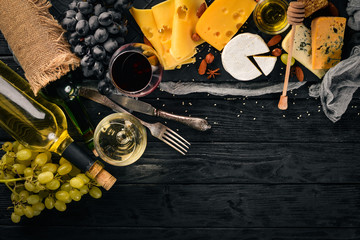 A large assortment of cheeses, brie cheese, gorgonzola, blue cheese, grapes, honey, nuts, red and white wine, on a wooden table. Top view. Free space for text.
