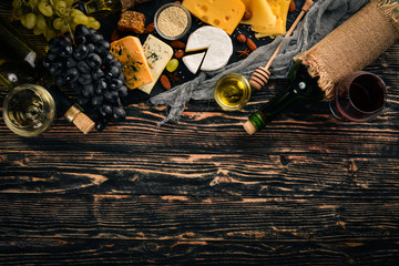 A large assortment of cheeses, brie cheese, gorgonzola, blue cheese, grapes, honey, nuts, red and white wine, on a wooden table. Top view. Free space for text.