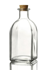 Empty transparent glass bottle of a square shape with a cork stopper on a reflective surface,...