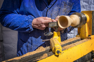 man's hands hold chisel near lathe, man working at small wood lathe, an artisan carves a piece of...