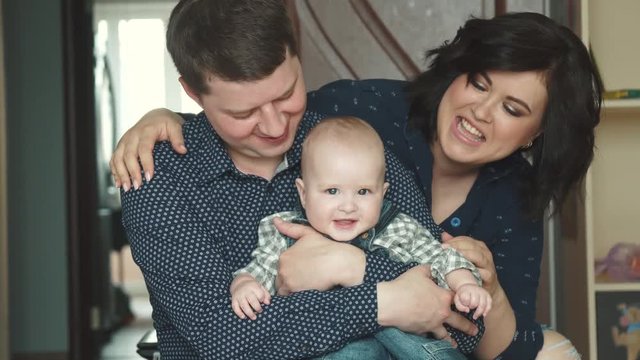 young father holds his young son in his arms. a child of 1 year old is sitting on his father's lap. mom, dad and a little son together. portrait of a happy family