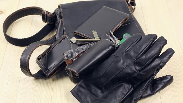 Leather goods for men. The man came home and lays down his leather accessories on a wooden table, a bag, a key case, a parole wallet, gloves, a watch