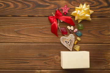 A beige box,a heart-shaped gingerbread, a red bow, a gold metallic bow and colored candies on a rustic wooden table. Christmas background. Copy space. Top view