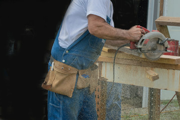 Sawdust flies as the end of the board the carpenter is cutting drops to the ground.