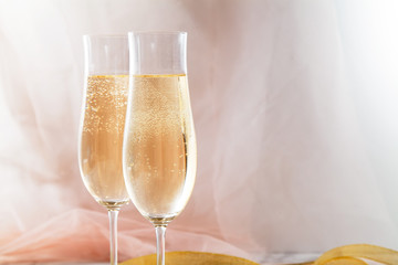 Two flute glasses with champagne on marble background. Pink transparent fabric. Soft light. Horizontal composition