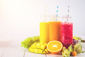 Multicolored smoothies in bottles of mango, orange, banana, celery, berries, on a wooden table.