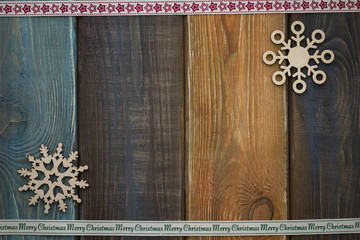 A colored wooden Christmas background with wooden snowflakes. A star patterned ribbon at the top. A Merry Cristmas inscription ribbon on the bottom. Copy space. Top view