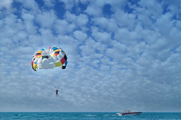 Fototapeta na wymiar Parasailing is above the sea. Focus on a parachute. Blue sky with small cumulus clouds